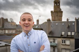 Photo dehors de Maxence Roger avec en arrière plan la Porte Horloge de Vire